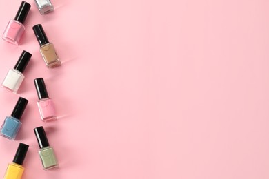 Pastel nail polishes in bottles on pink background, flat lay. Space for text