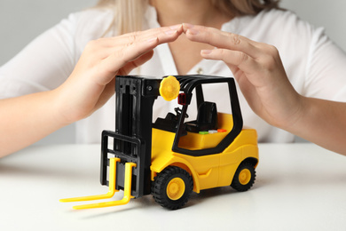 Photo of Woman covering toy forklift at white table, closeup. Logistics and wholesale concept