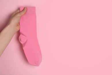 Photo of Woman holding sock on light pink background, closeup. Space for text