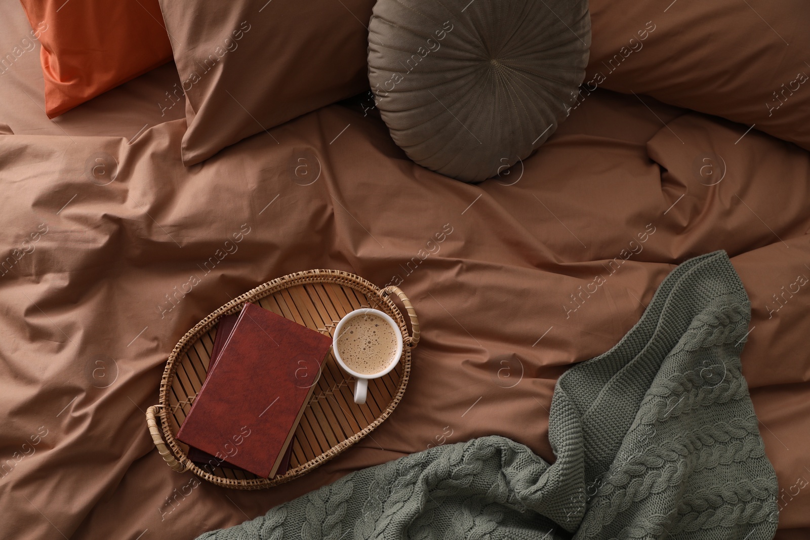 Photo of Cup of hot coffee and books on bed with stylish linens, above view