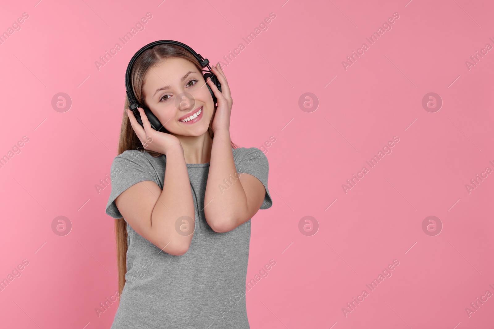 Photo of Teenage girl listening to music with headphones on pink background. Space for text