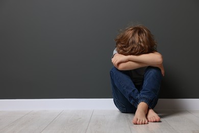 Photo of Child abuse. Upset boy sitting on floor near grey wall, space for text