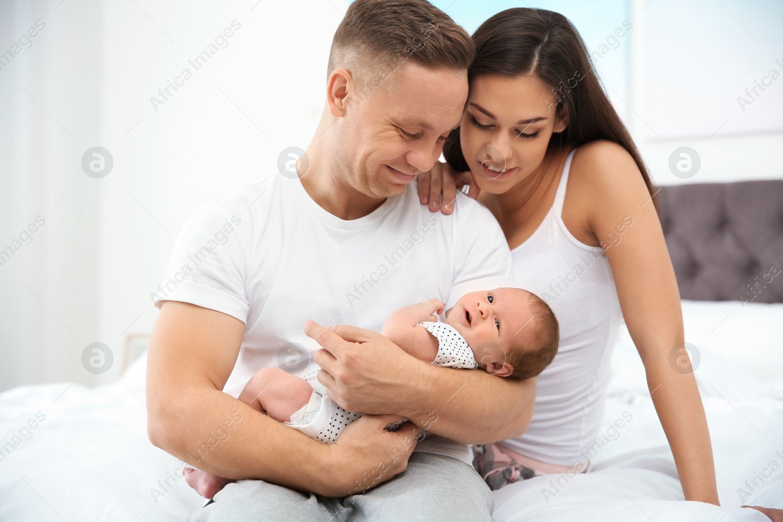 Photo of Happy couple with their newborn baby on bed