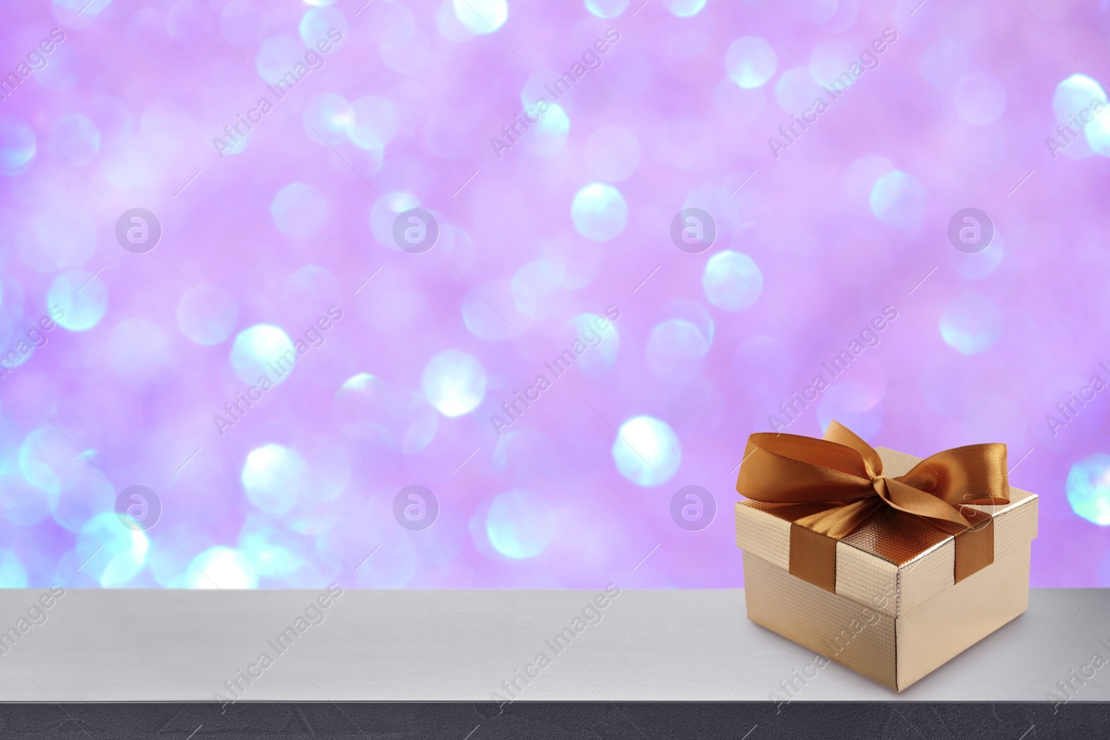 Image of Beautiful gift box on white table against blurred festive lights, bokeh effect. Space for text