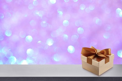 Beautiful gift box on white table against blurred festive lights, bokeh effect. Space for text