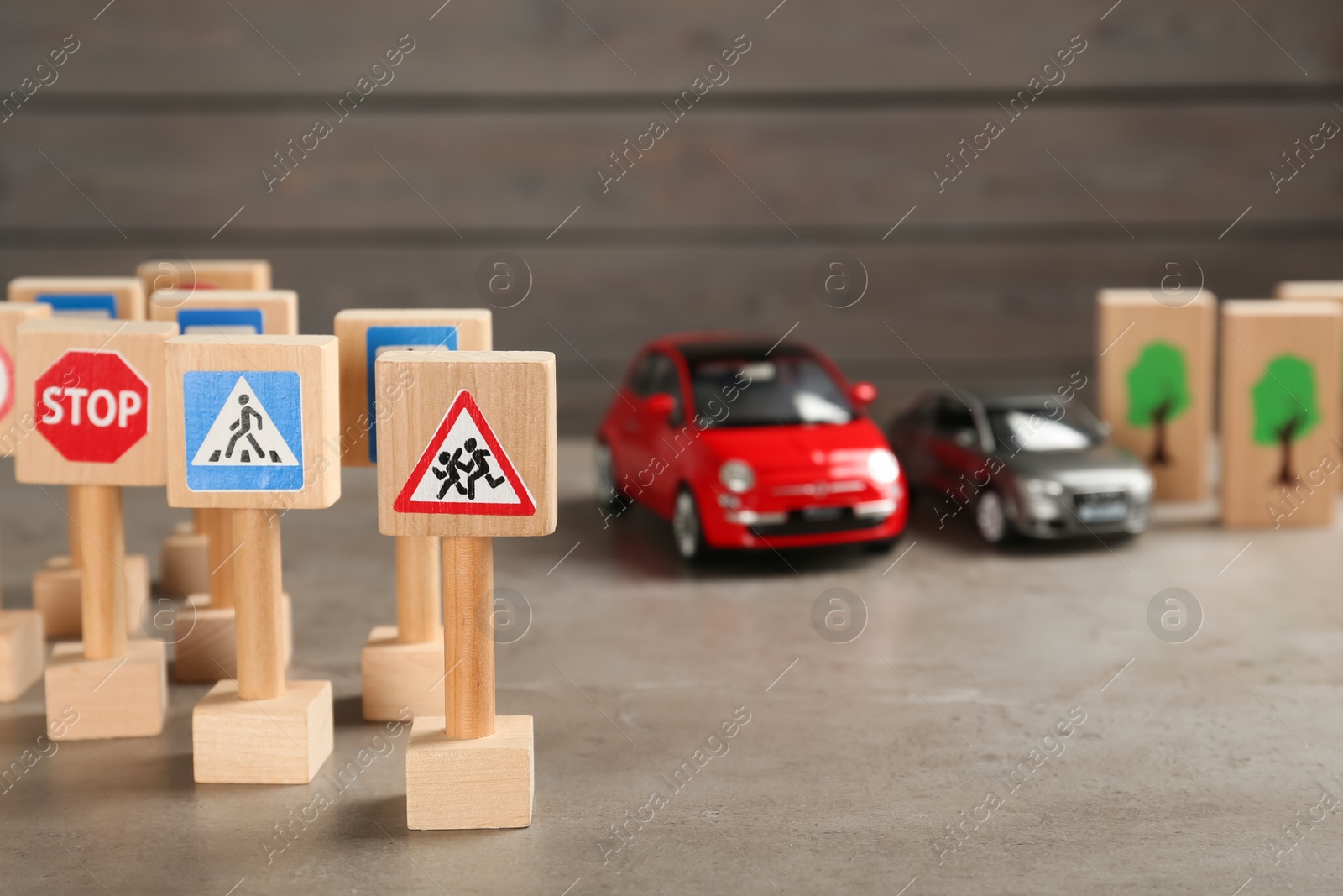 Photo of Many different miniature road signs and cars on grey table, space for text. Driving school