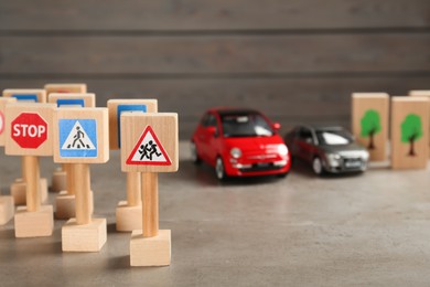 Photo of Many different miniature road signs and cars on grey table, space for text. Driving school