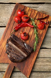 Board with delicious grilled beef meat with vegetables and rosemary on wooden table, top view