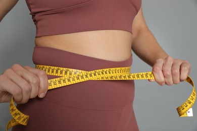 Photo of Woman measuring waist with tape on grey background, closeup