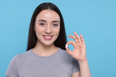 Photo of Beautiful young woman showing pill on light blue background. Space for text