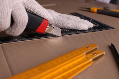 Photo of Worker cutting cardboard with utility knife and ruler, closeup