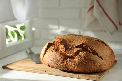 Photo of Freshly baked sourdough bread and knife on white wooden table indoors