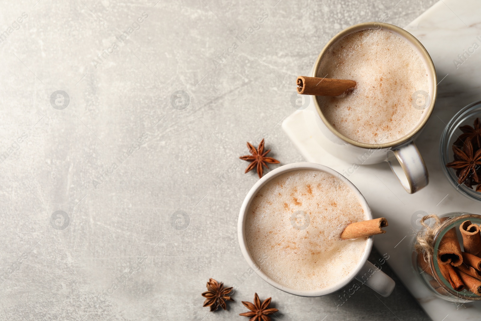 Photo of Cups of delicious eggnog with anise and cinnamon on light grey table, flat lay. Space for text