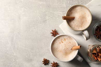 Cups of delicious eggnog with anise and cinnamon on light grey table, flat lay. Space for text