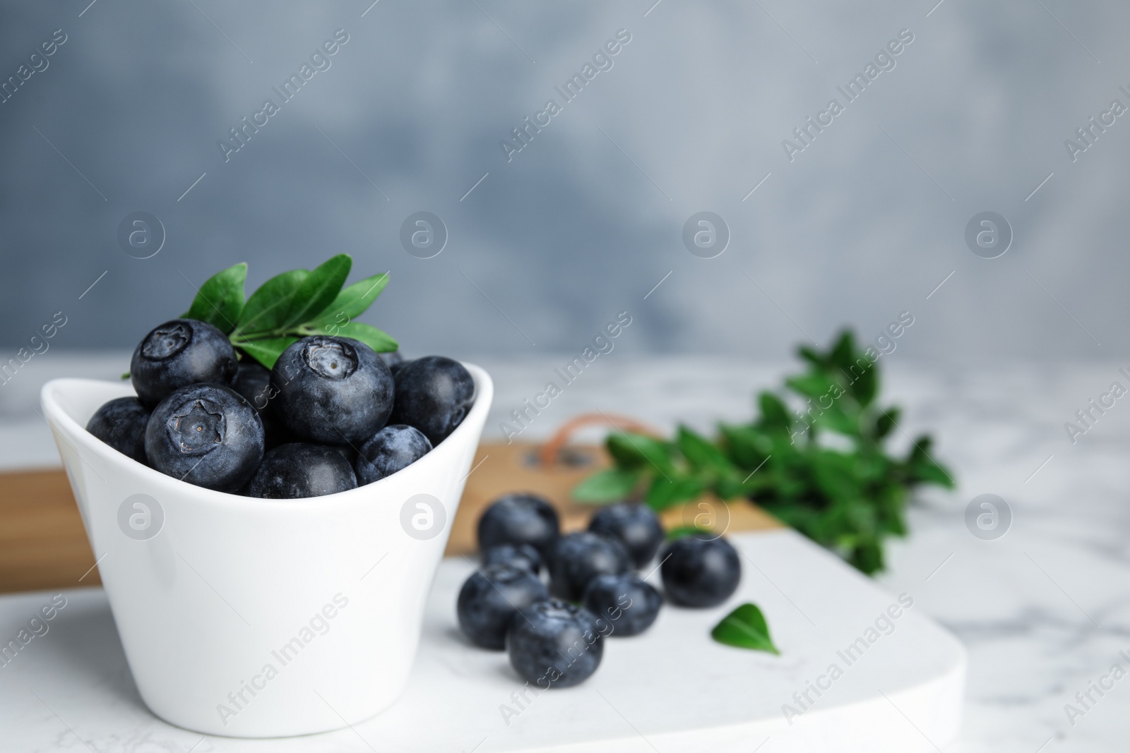 Photo of Board with bowl of tasty fresh blueberries on table against color background, space for text