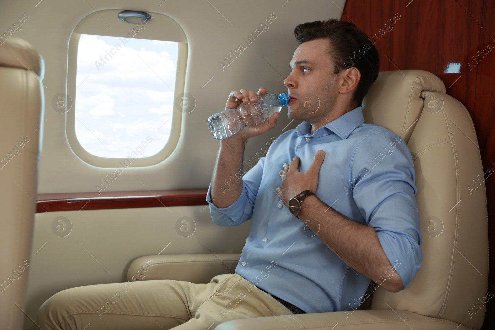Photo of Nervous young man with aviophobia drinking water in airplane