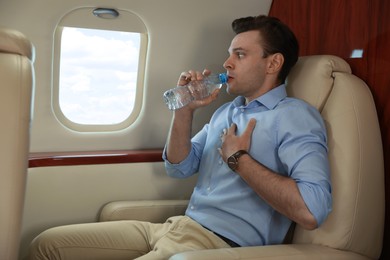 Nervous young man with aviophobia drinking water in airplane