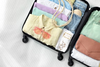 Photo of Open suitcase full of clothes and accessories on white blanket, top view