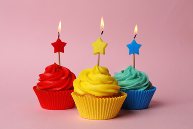 Photo of Delicious birthday cupcakes with burning candles on pink background