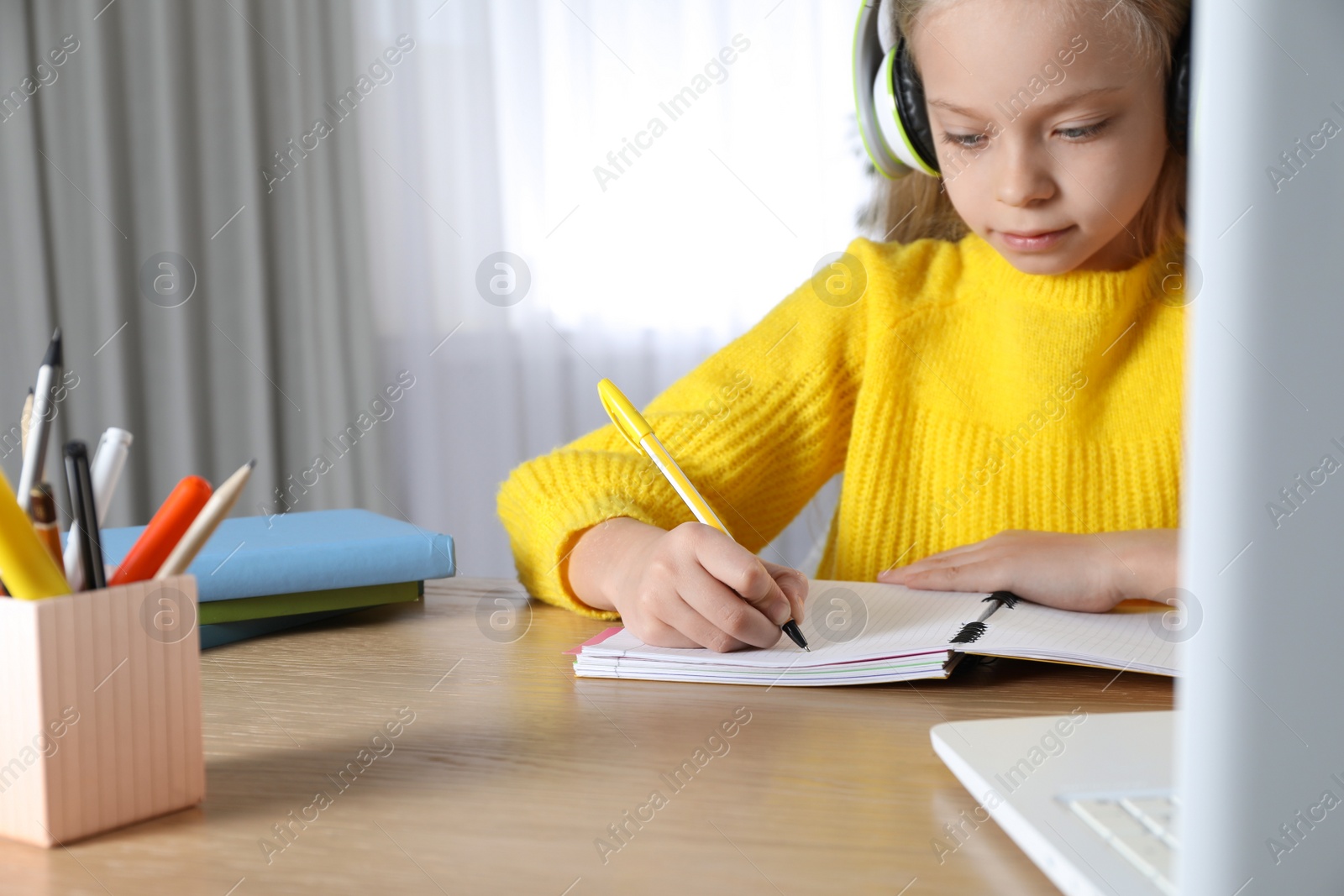 Photo of Cute little girl with laptop studying online at home, space for text. E-learning