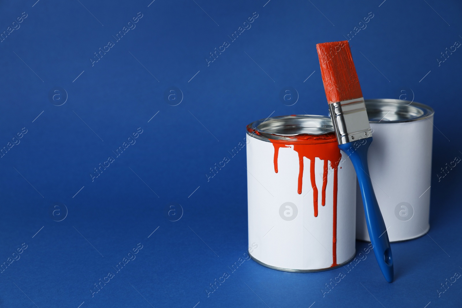 Photo of Cans of orange paint and brush on blue background. Space for text
