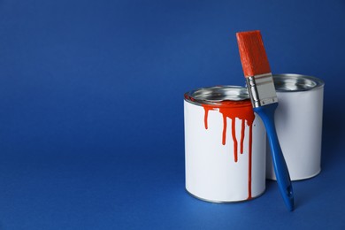 Cans of orange paint and brush on blue background. Space for text