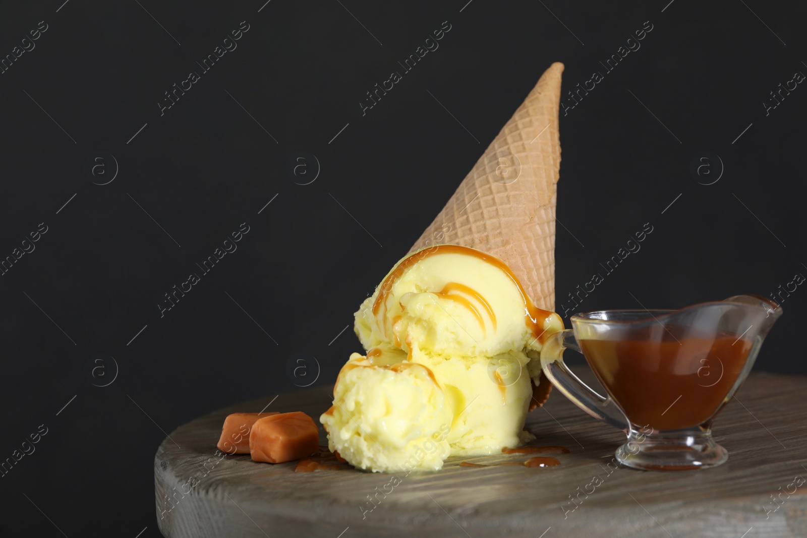 Photo of Delicious yellow ice cream with syrup in wafer cone and caramel candies on table. Space for text