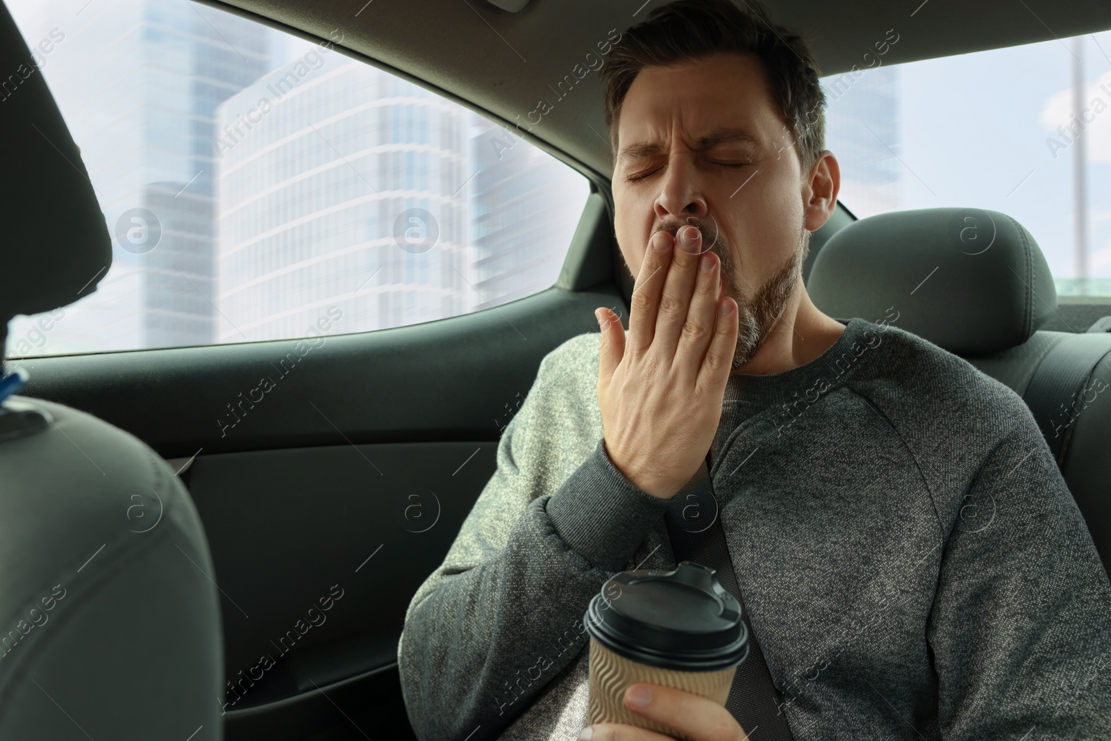 Photo of Sleepy man with cup of coffee yawning in modern car