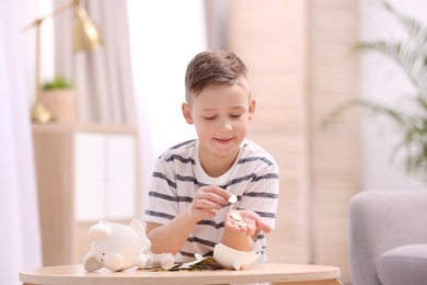 Photo of Little boy with broken piggy bank and money at home