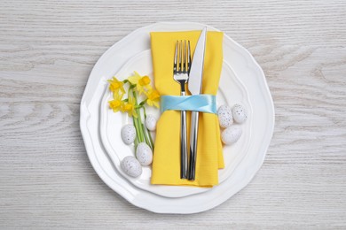 Photo of Festive table setting with painted eggs and cutlery on white wooden background, top view. Easter celebration