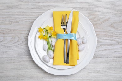 Festive table setting with painted eggs and cutlery on white wooden background, top view. Easter celebration