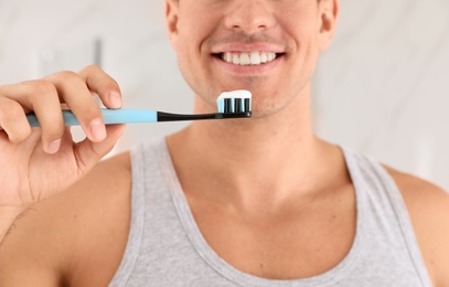 Photo of Man holding toothbrush with paste indoors, closeup