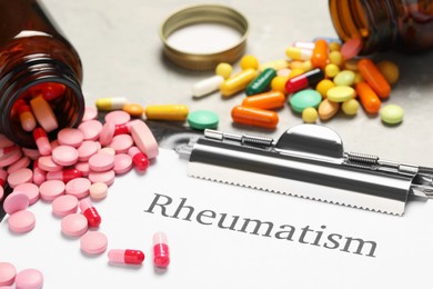 Photo of Clipboard with word Rheumatism and pills on table, closeup