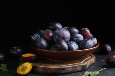Delicious ripe plums on table against black background