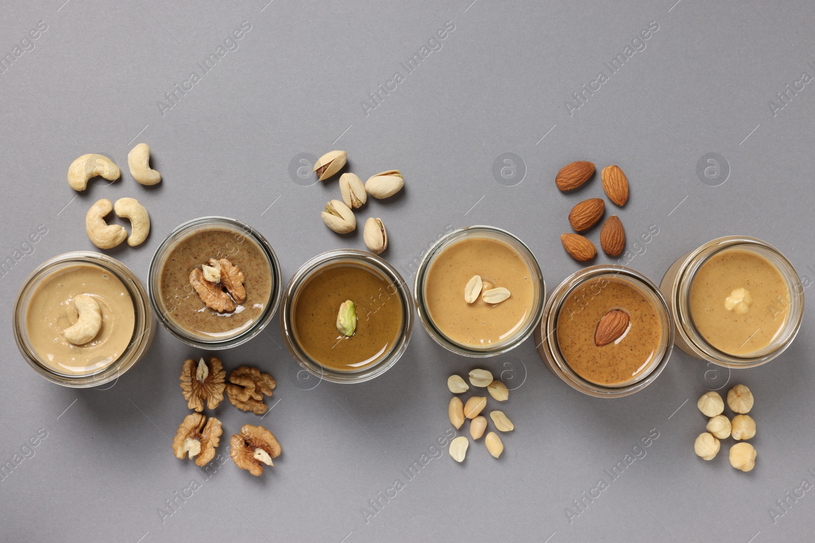 Photo of Tasty nut butters in jars and raw nuts on gray table, flat lay