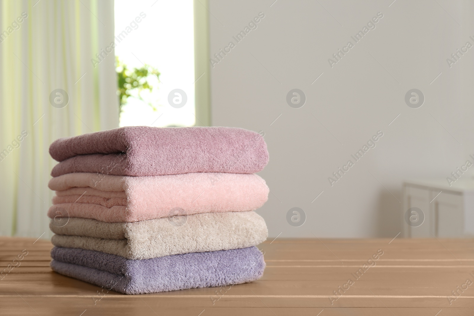 Photo of Stack of fresh towels on wooden table in bathroom. Space for text