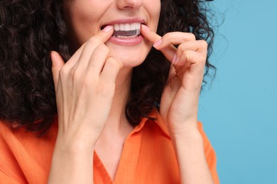 Young woman applying whitening strip on her teeth against light blue background, closeup. Space for text
