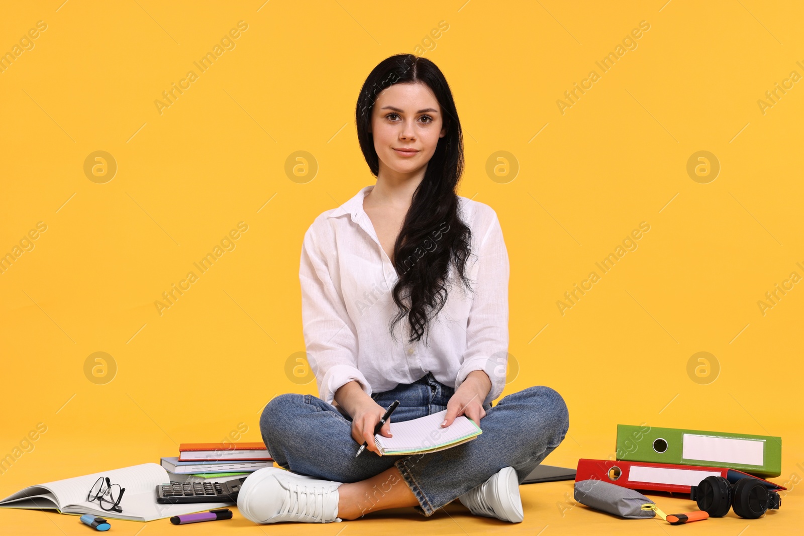 Photo of Student with notebook sitting among books and stationery on yellow background