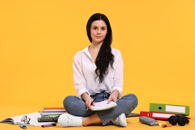 Photo of Student with notebook sitting among books and stationery on yellow background