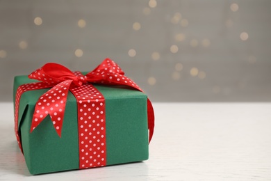 Photo of Beautifully wrapped gift box on white wooden table against blurred festive lights, space for text
