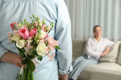 Photo of Man hiding bouquet of flowers for his beloved woman indoors, closeup