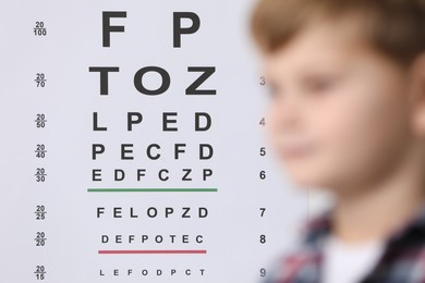 Photo of Cute little boy against vision test chart, selective focus