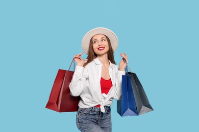 Stylish young woman with shopping bags on light blue background