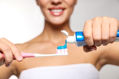 Photo of Woman applying toothpaste on brush against light background, closeup