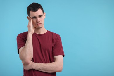 Portrait of sad man on light blue background, space for text