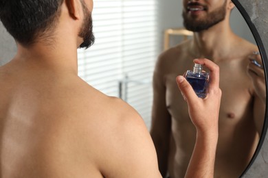 Man spraying luxury perfume near mirror indoors, closeup