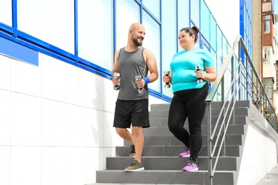 Overweight man and woman running with dumbbells on stairs outdoors