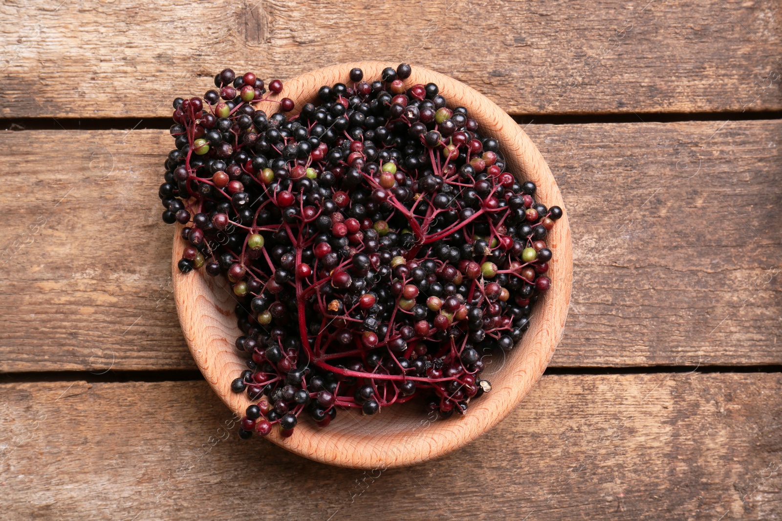 Photo of Bowl with tasty elderberries (Sambucus) on wooden table, top view
