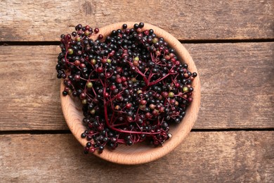Photo of Bowl with tasty elderberries (Sambucus) on wooden table, top view