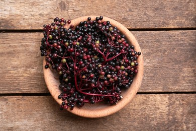 Bowl with tasty elderberries (Sambucus) on wooden table, top view